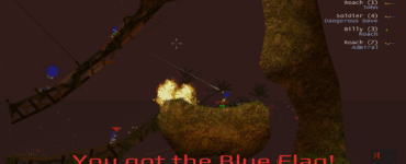 2D-gameplay fra Soldat, hvor en spiller bærer den blå flag på et skovlignende map. Eksplosioner lyser området op, mens flere spillere kæmper på træbroer og klippeformationer. HUD’en viser health, ammo og jet-fuel nederst, og scoreboardet ses til højre.