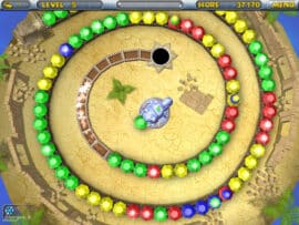 Skærmbillede fra Chameleon Gems, hvor spilleren skyder farvede perler mod en spiralførende kæde for at lave match-3 kombinationer på en sanddækket bane.