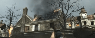 Skærmbillede fra vores test af Call of Duty: World at War, hvor spilleren sigter med et WWII-gevær mod en brændende bygning i en bombet by med kraftig røg og ild.