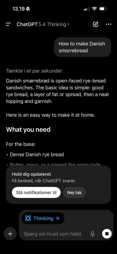 Skærmbillede af ChatGPT 5.4 Thinking på iPhone i mørk tilstand, hvor appen viser et svar på spørgsmålet om dansk smørrebrød samt en notifikationspopup nederst på skærmen.