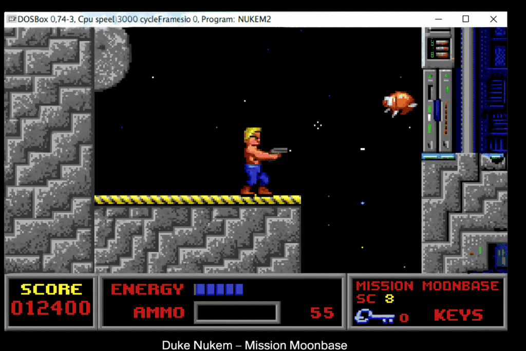 Screenshot fra vores test af Duke Nukem – Mission Moonbase, hvor Duke står på en månebaseplatform og skyder mod en flyvende robot i klassisk pixelgrafik fra DOS-æraen.
