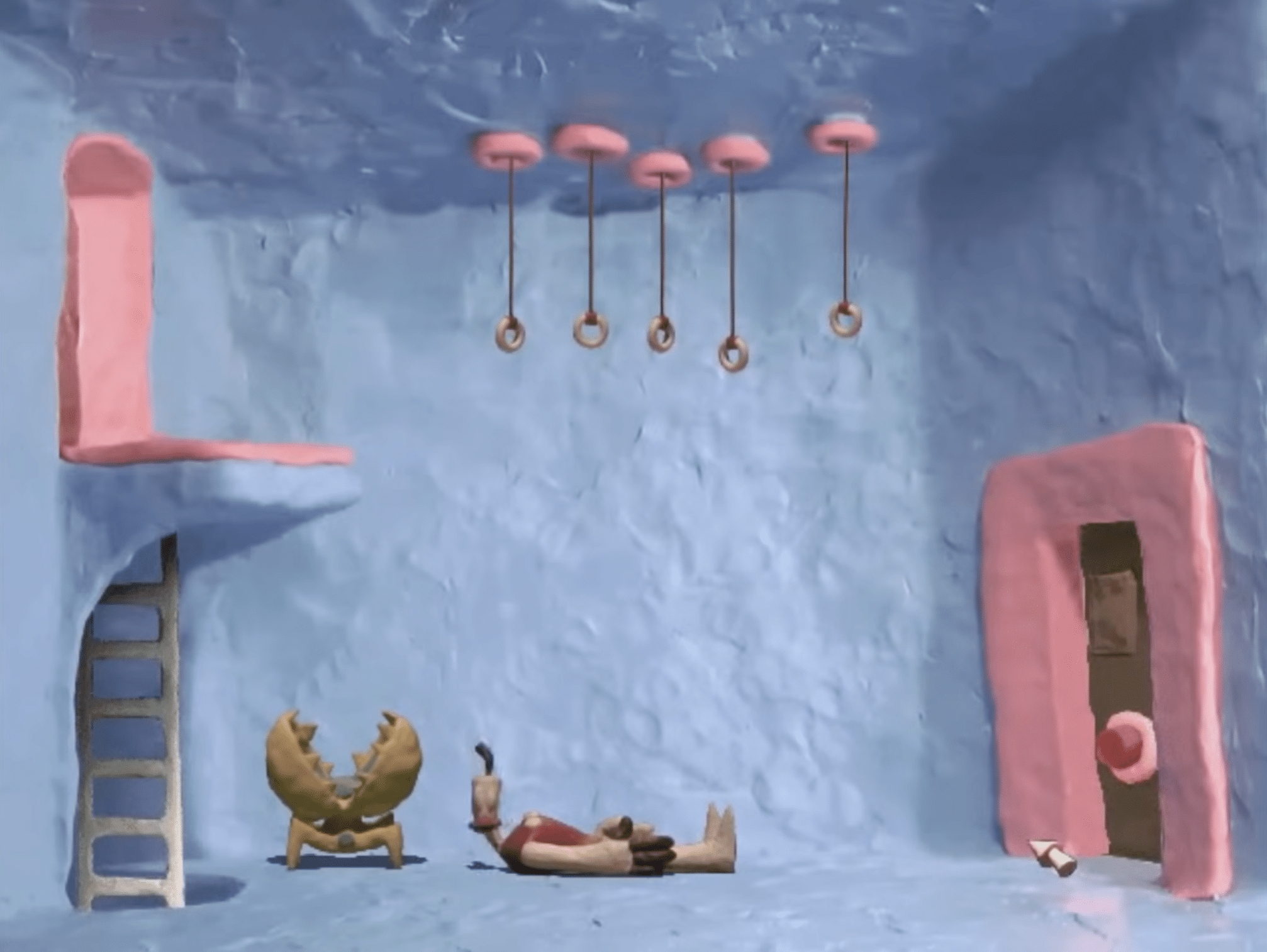 Klaymen lies on the floor in a blue clay room in The Neverhood, surrounded by a ladder, hanging rings, a crab-like chair, and a pink door.