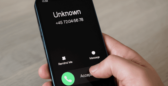 En hånd holder en smartphone, der viser et indgående opkald fra et ukendt nummer med teksten "Unknown" og et dansk telefonnummer, klar til at blive besvaret eller afvist.