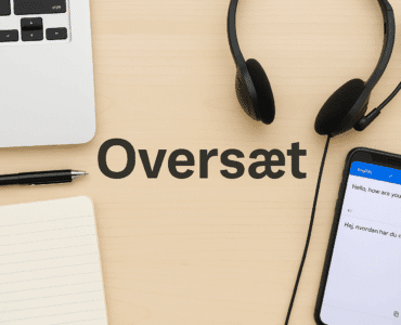 Et skrivebord med oversættelsesværktøjer – en bærbar computer, notesbog, kuglepen, headset og en smartphone med oversættelsesapp – med ordet "Oversæt" skrevet i midten på træoverfladen.