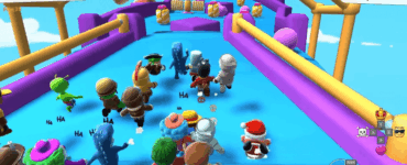 Skærmbillede fra Stumble Guys, hvor flere farverige figurer løber mod målstregen på en forhindringsbane med bevægelige platforme og kanoner i baggrunden.