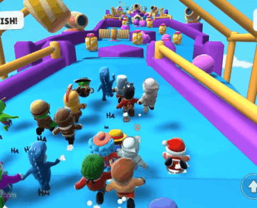 Skærmbillede fra Stumble Guys, hvor flere farverige figurer løber mod målstregen på en forhindringsbane med bevægelige platforme og kanoner i baggrunden.