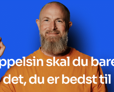 Mand med skæg holder en appelsin foran blå baggrund – Appelsin er en dansk regnskabsapp for selvstændige og små virksomheder