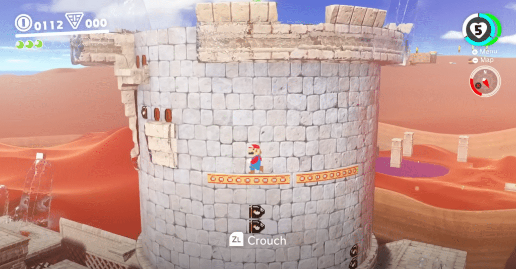 Mario udforsker en ørkenverden i Super Mario Odyssey, hvor han står på en platform på siden af et stort rundt stentårn.